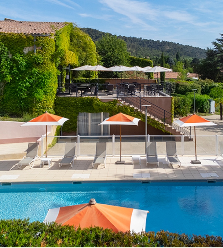 Vue apaisante de la piscine de l'Hôtel Lou Paradou, entourée de chaises longues confortables et de parasols orange. Le cadre verdoyant et les terrasses ensoleillées créent une atmosphère relaxante, idéale pour les séjours bien-être. Cet hôtel de Provence est le choix parfait pour les visiteurs cherchant à se ressourcer dans un environnement naturel paisible.