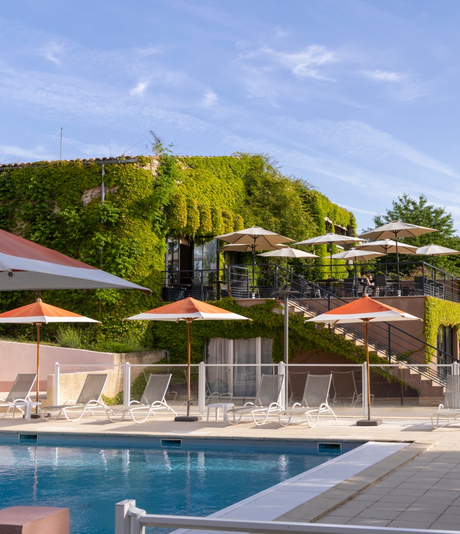 Piscine relaxante du Lou Paradou Hotel, entourée de chaises longues confortables et de parasols, avec une vue sur le jardin verdoyant. L'espace extérieur invite à la détente, parfait pour les visiteurs cherchant un séjour paisible en Provence. Les escaliers mènent à une terrasse où les clients peuvent se restaurer dans une atmosphère sereine, mettant en avant le cadre naturel et le bien-être.