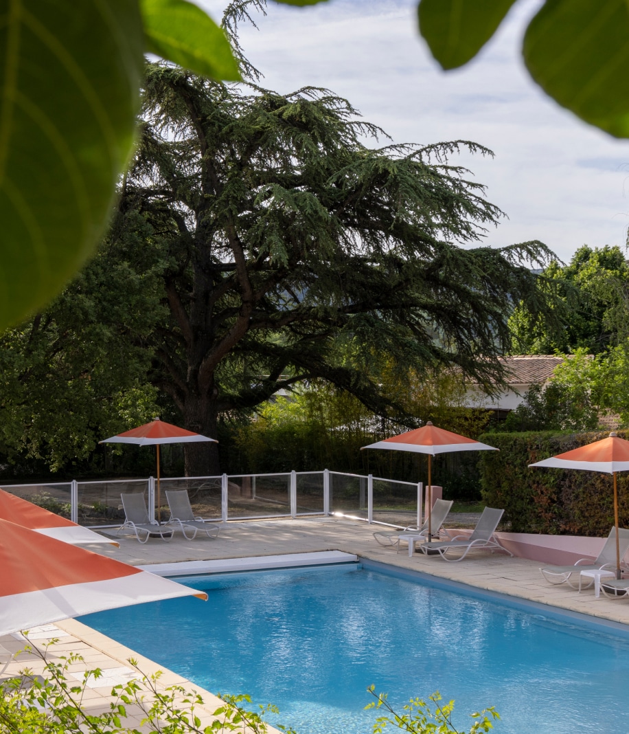 Profitez d'une vue apaisante sur la piscine de l'Hôtel Lou Paradou, entourée d'une végétation luxuriante et équipée de chaises longues confortables. Les parasols orange ajoutent une touche de couleur à cet espace de détente, parfait pour se relaxer après une journée d'exploration en Provence. Cet hôtel, reconnu pour son cadre naturel et son ambiance sereine, offre une expérience de bien-être inégalée, idéale pour les amateurs de spa et de